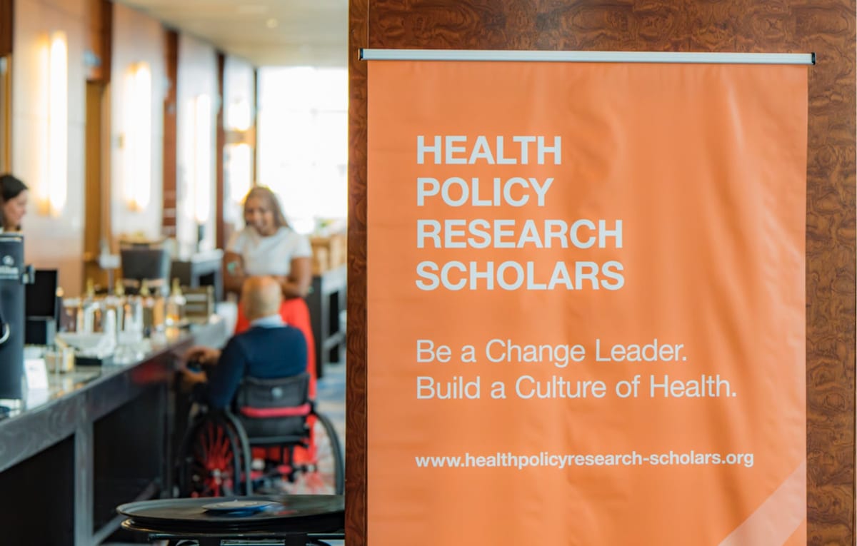 Health Policy Research Scholars banner beside scholars gathering in an accessible event space