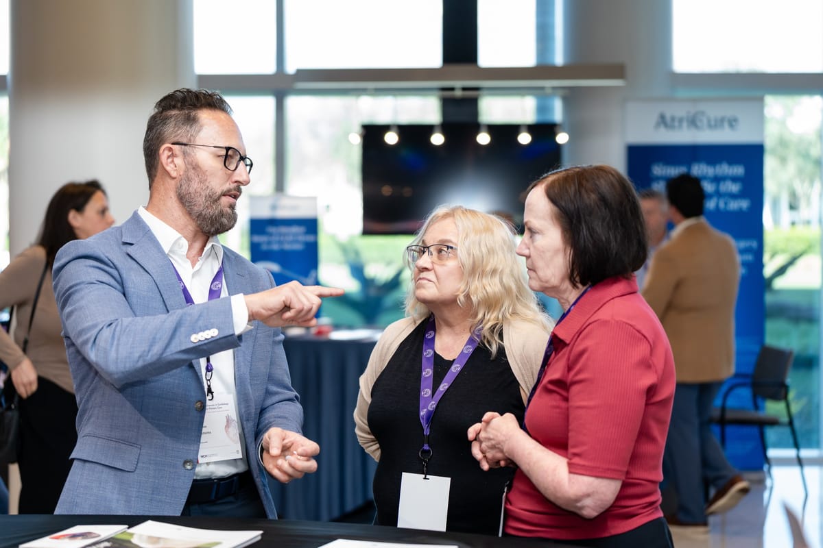 Sponsor representative speaking with two attendees on the Naples Cardiovascular Summit exhibitor floor