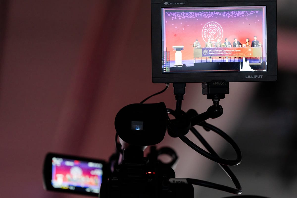 Video camera recording a summit panel with the stage visible on its monitor