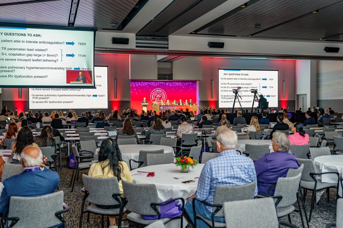 Wide Naples Cardiovascular Summit general session with the audience, stage, screens, and production cameras visible