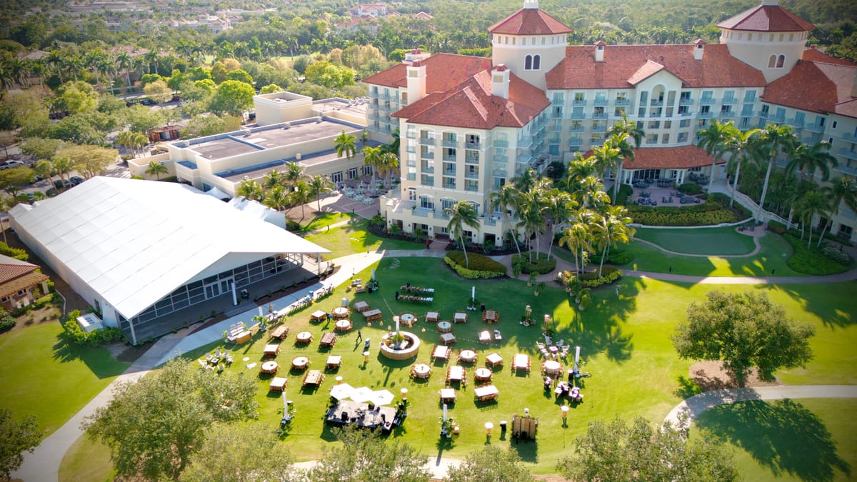 Aerial view of a resort lawn prepared with event tables, a stage, and a large hospitality tent