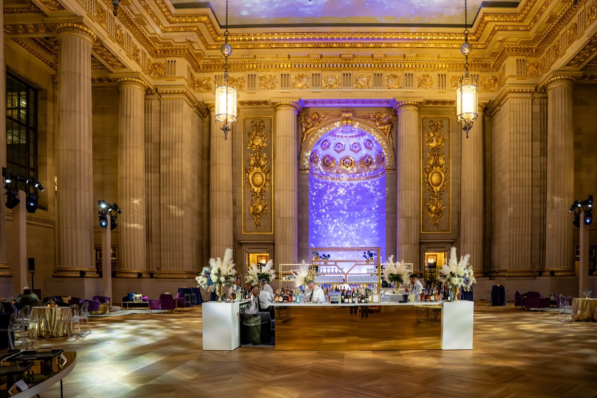 Ornate ballroom prepared for dinner with gold architectural details and a violet-lit focal wall