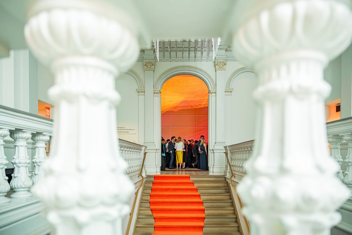 Guests framed at the top of a vivid orange carpet inside a white marble venue