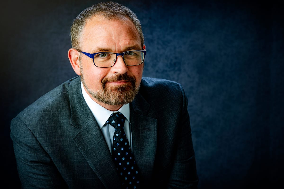 Executive headshot with directional light against a deep blue-grey background