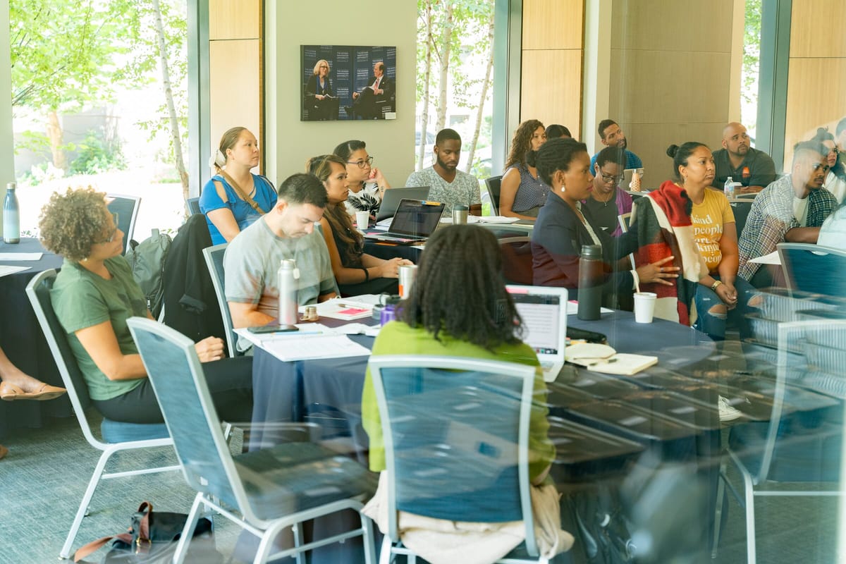 Scholars in a working session around conference tables, photographed through glass